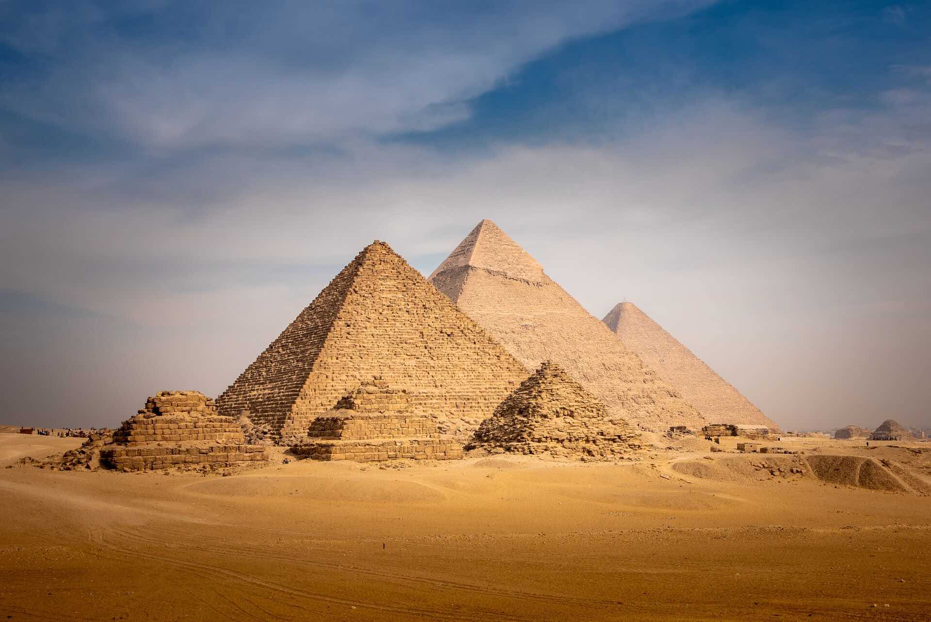 A wide andlge shot of the Great Pyramids of Giza, surrounded by sand.