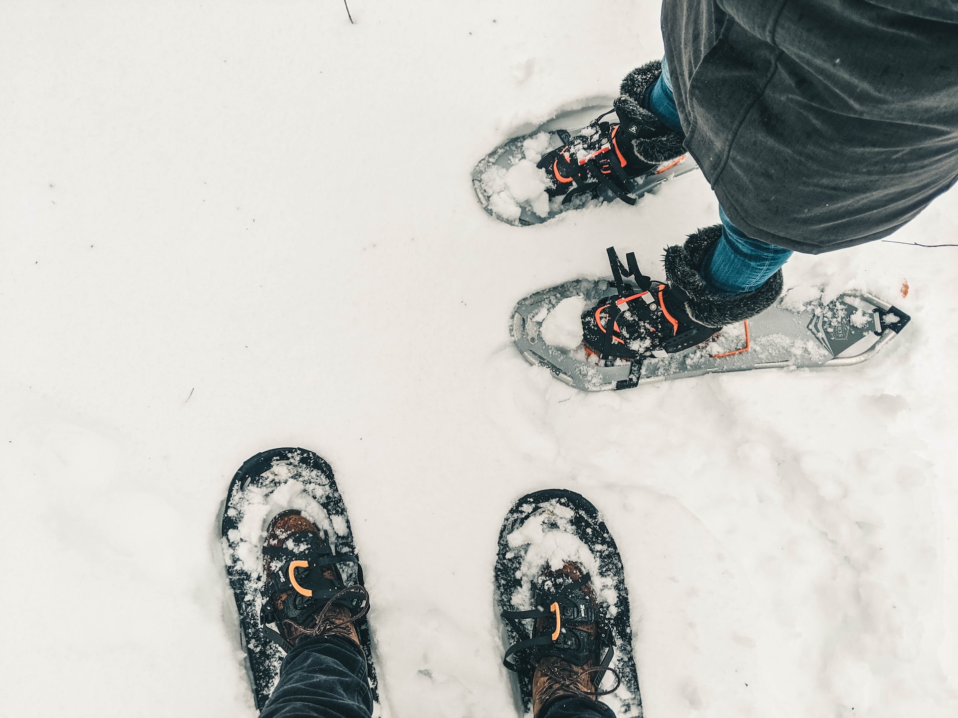 An image of two peoples' snowshoes, shot from a POV angle looking down at feet in the snow