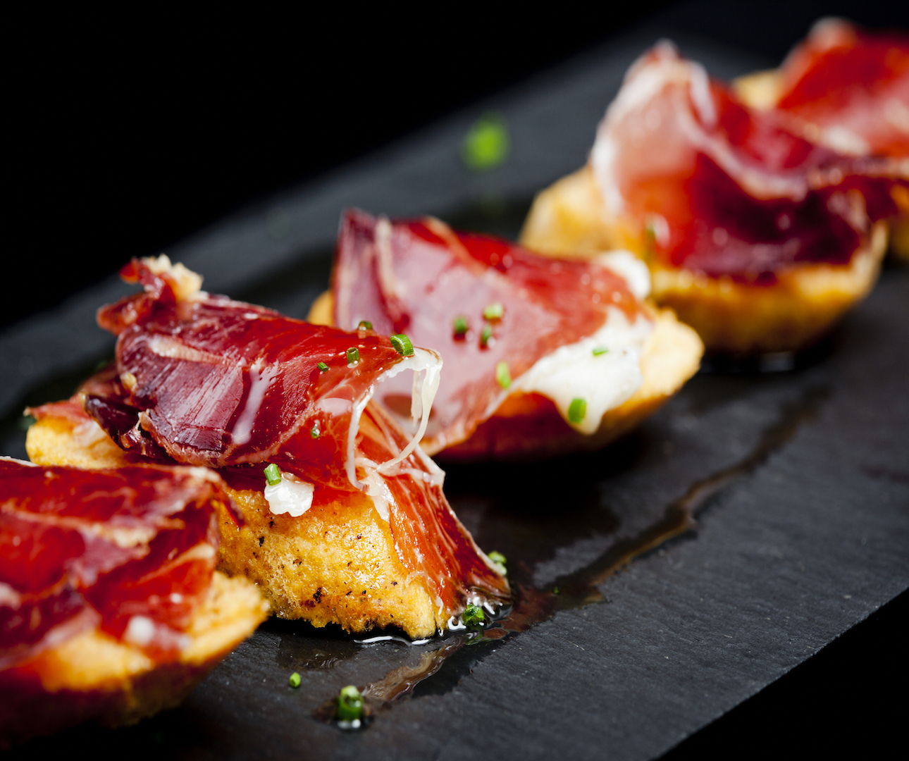 Closeup of fried tapas dish with iberico ham on top. If you're wondering how to Order Food in Spain, this is the perfect dish to get