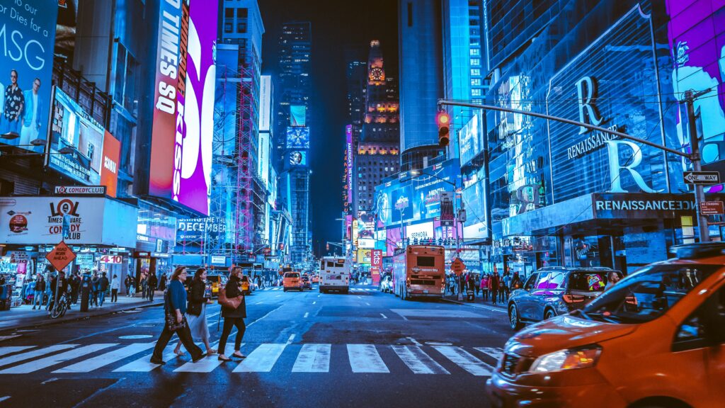 The lights if Times Square in New York, with cars and people crossing the cross walk. 
