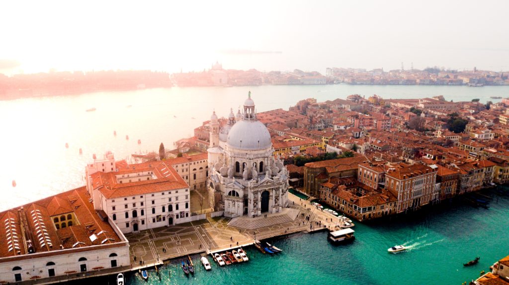 Ornate buildings in Venice, Italy surrounded by green water and a hazy sunset