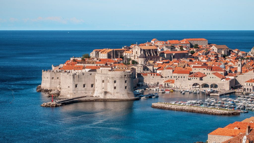 Red roofs adorn the walled city of Dubrovnik, Croatia with bright blue waters leading to the skyline.