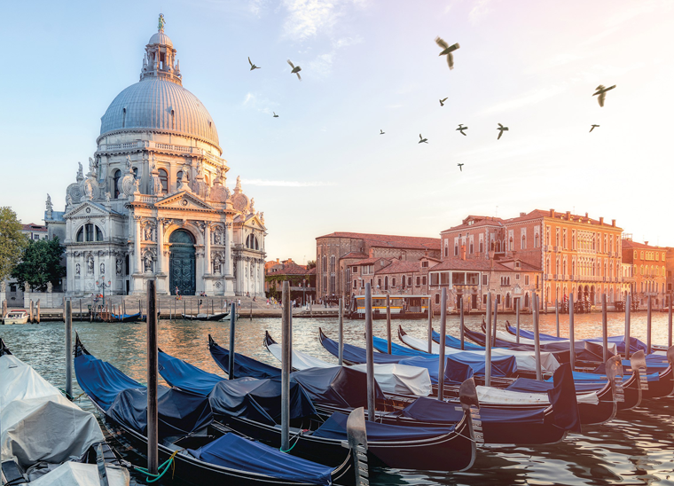 Gondolas line the canal in Vencie Italy, with a large domed church behind.