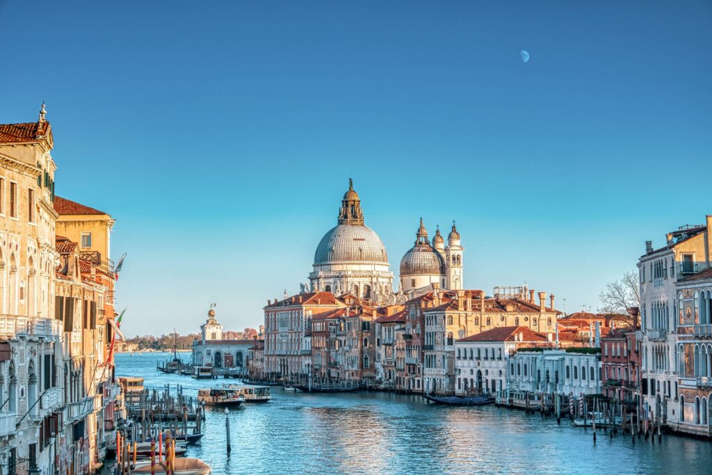 Grand buildings in Venice flank the bright blue canal in the morning sun.