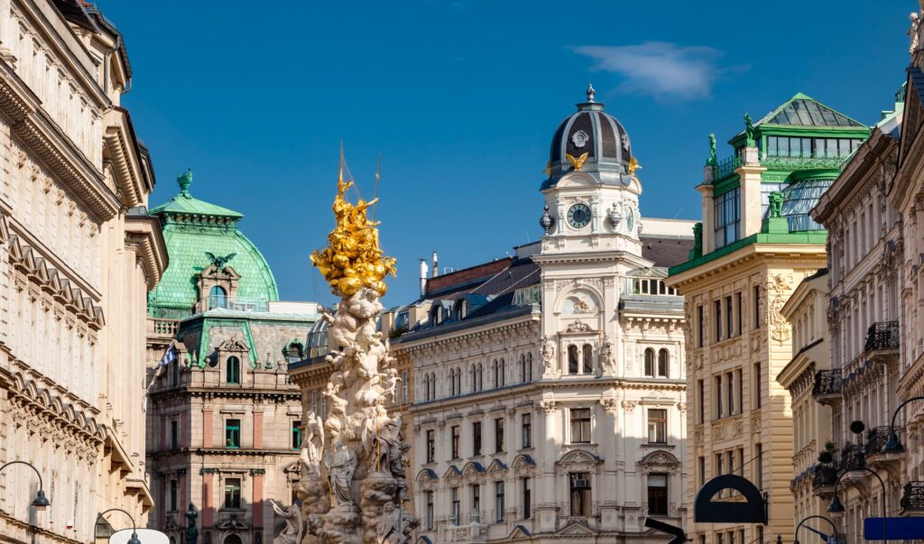 ornate buildings in Vienna, Austria with green domes roofs and a golden statue.