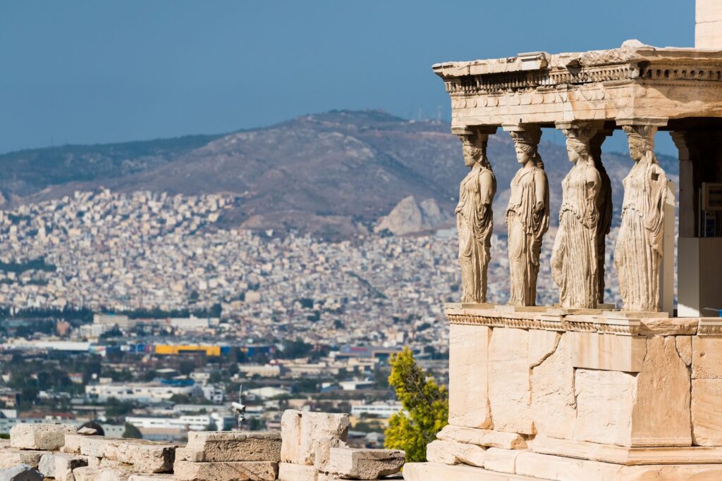 Four ancient statues at the Acropolis in Athens gaze out over the city and the mountains behind.