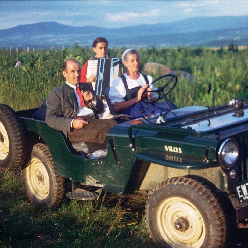 The Von Trapp Family in an open top car, driving through a field
