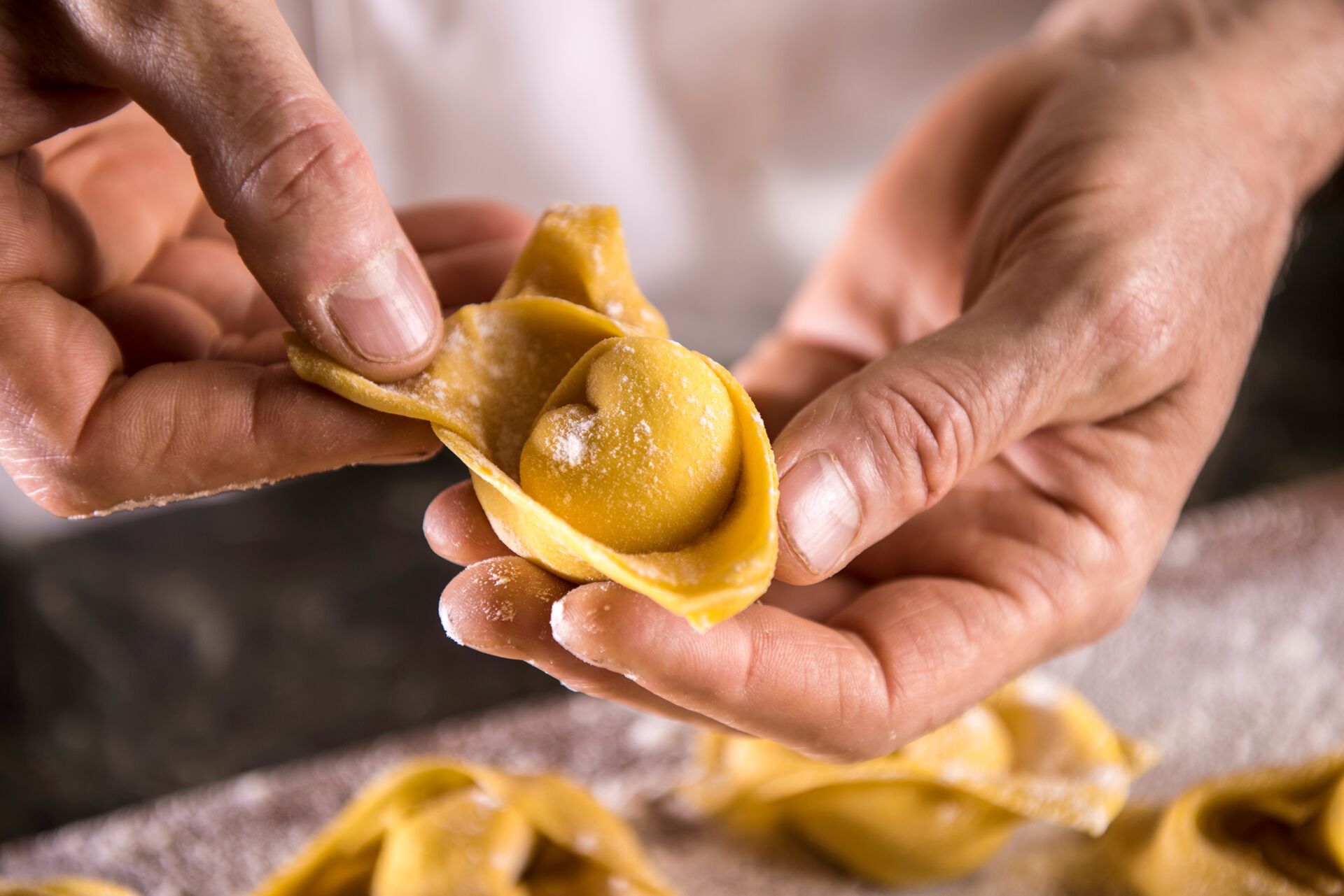 A close up of hands carefully rolling golden fresh pasta parcels