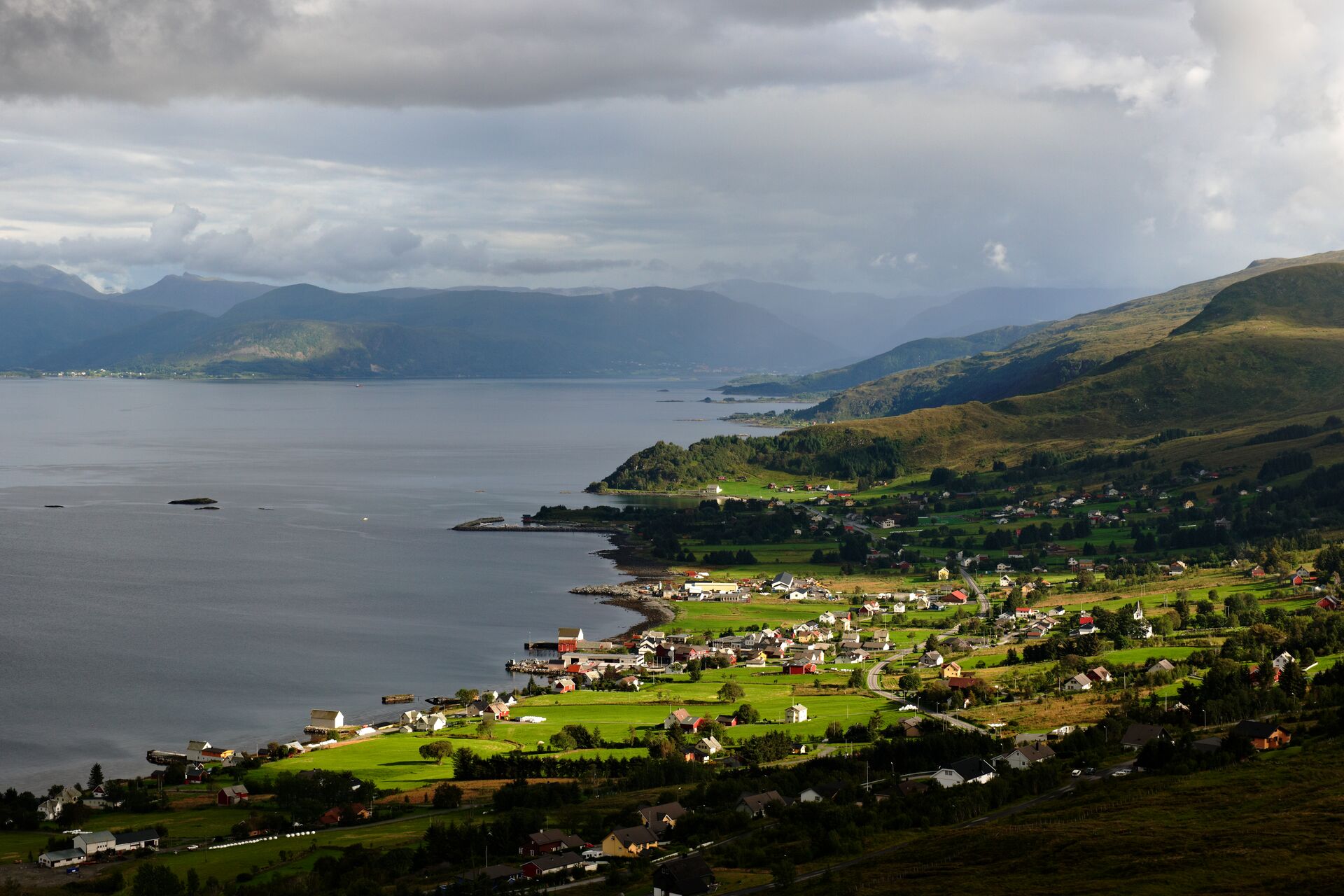 Aerial shot of a fjord side town with green fields and gloomy skies in Norway.