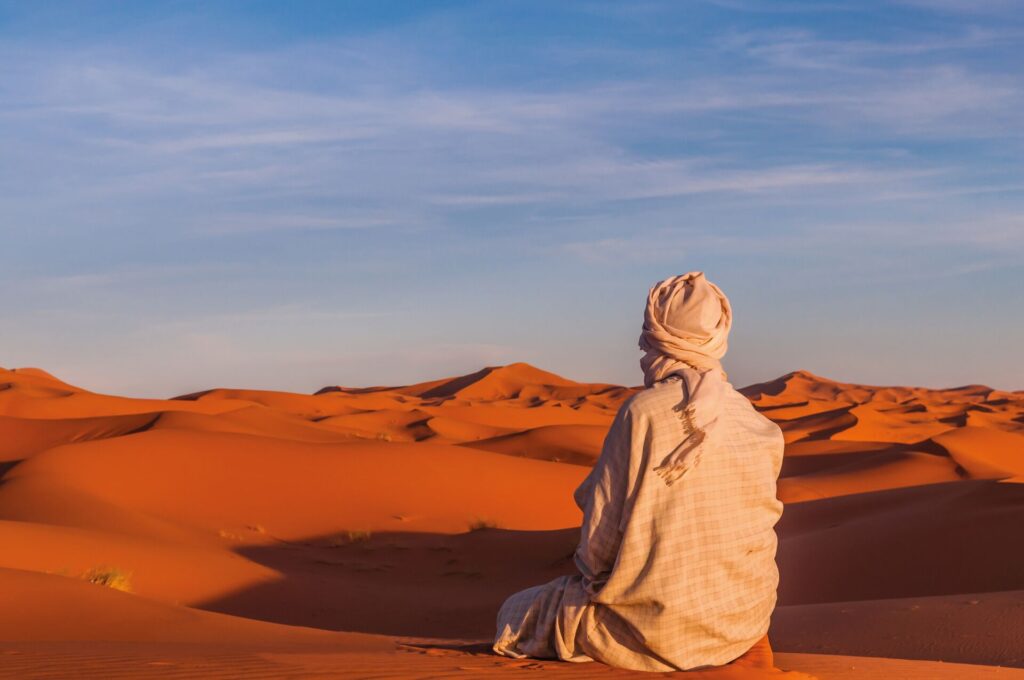 Image of Berber man sitting down, from behind as he overlooks the Sahara Desert