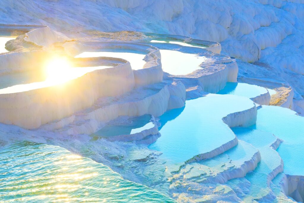 Sun glinting over the bright blue waters of thermal springs located on white limestone terraces, Pamukkale, Turkey
