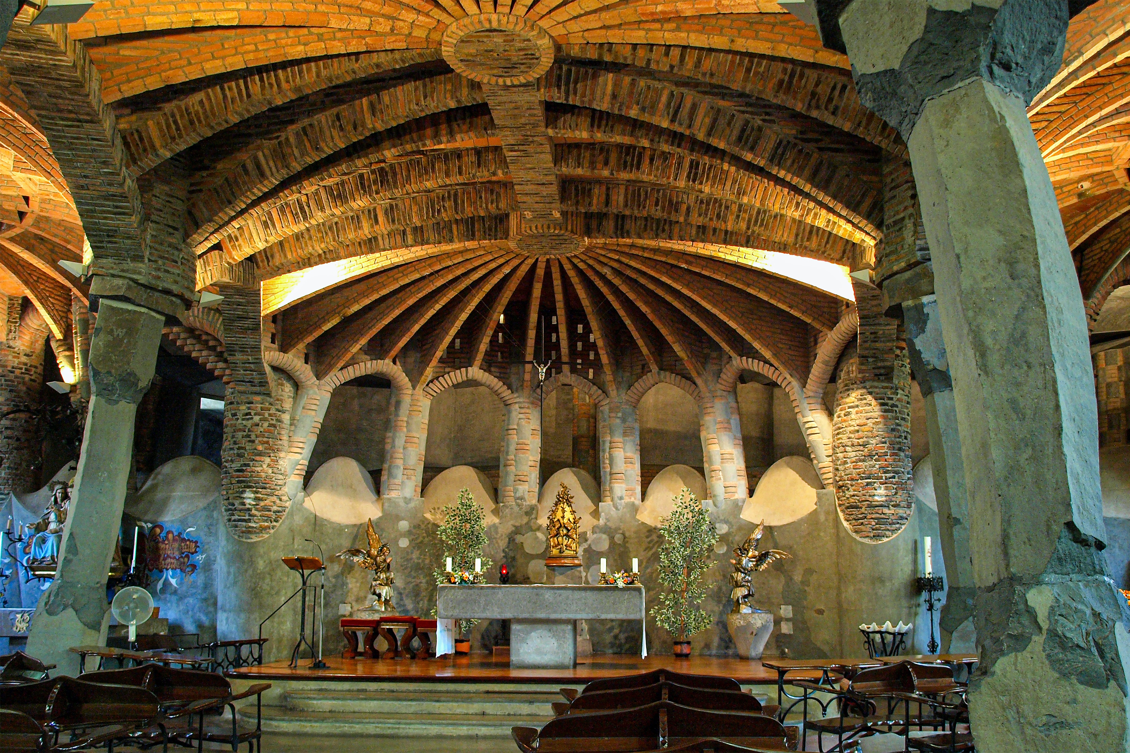 an altar with stone pillars and ornate roofing in Gaudi’s church Colonia Guell