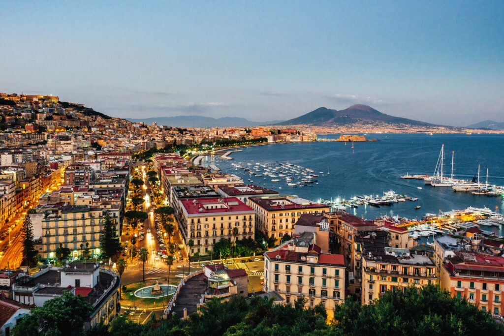 Aerial shot of Naples showing red roofed buildings, and the bay with a dark blue sea
