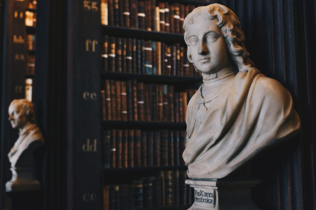 A bust of a man in front of books in a library, holding a guide to the Grand Canyon.