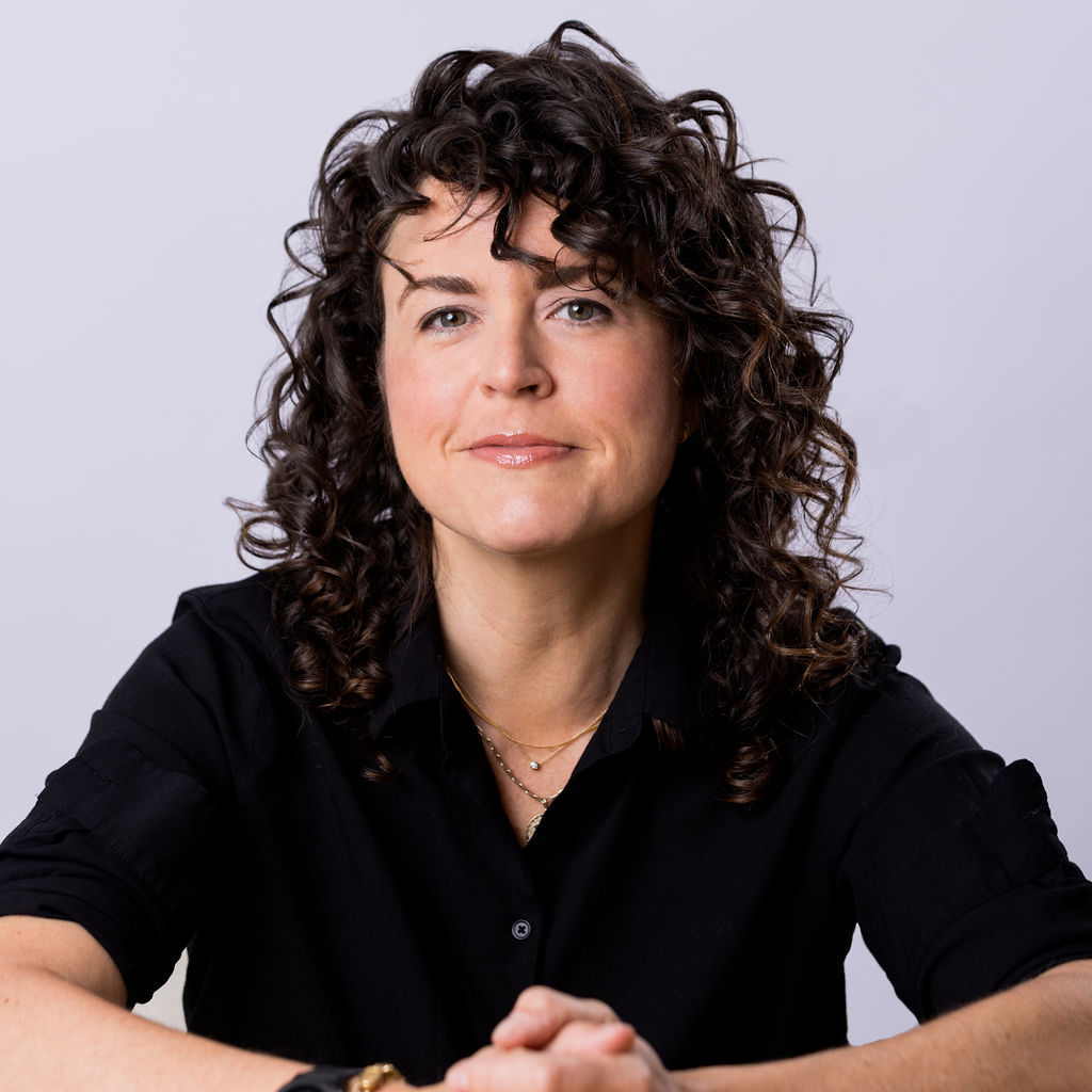 A sustainability specialist with curly hair sitting in front of a white background.