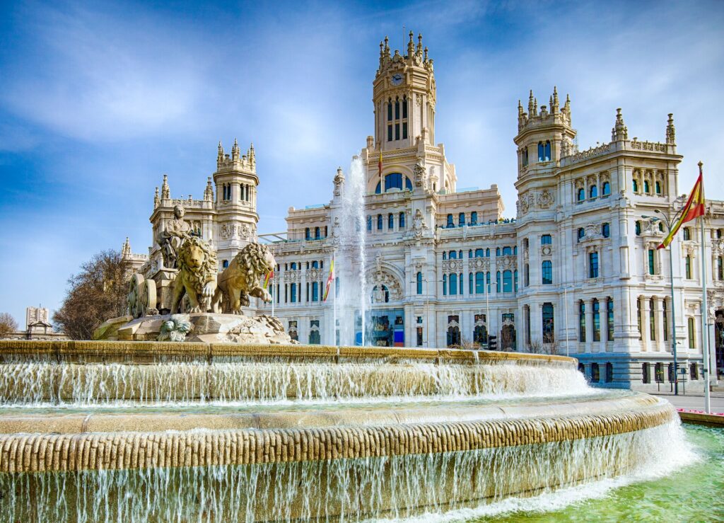 The white and gold Cibeles Fountain In Downtown Madrid, Spain with an ornate fountain in front