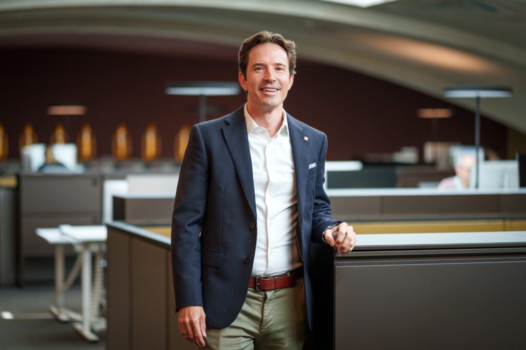 Portrait of Pascal Prinz wearing a white shirt under a blue blazer 