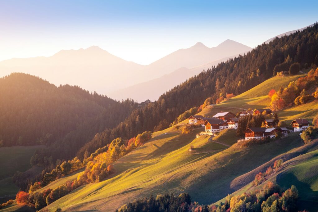 View of a hillside in the late afternoon sun, with fall-coloured trees and traditional chalet-style buildings