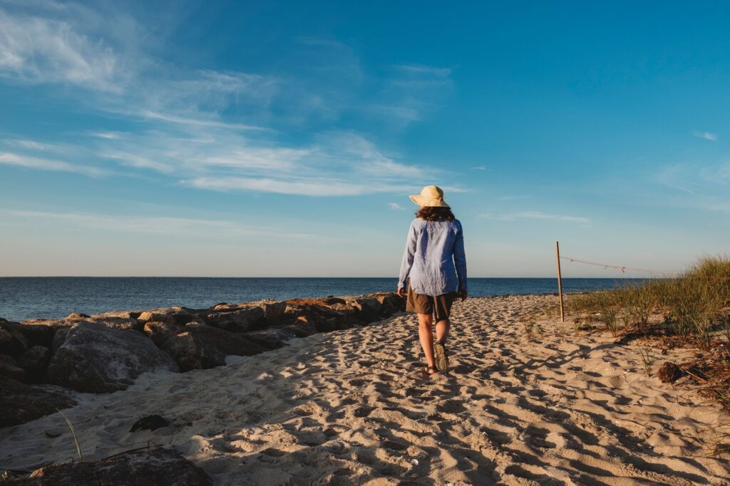 A woman walks on a sand path with the sea if front in Cape Cod, USA