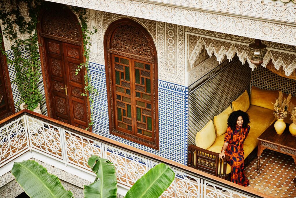 A woman sits in a courtyard of intricate tiles and wooden doors in Morocco