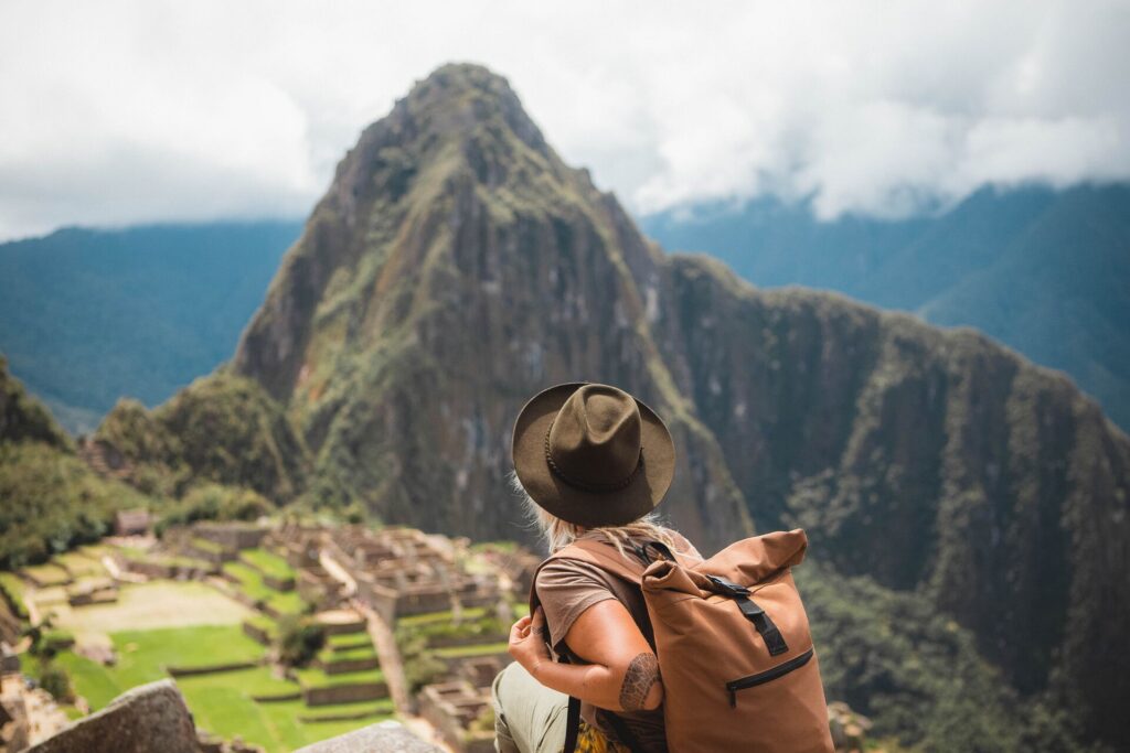 Rear view of woman looking at Machu Picchu in Peru against a blue sky with clouds.