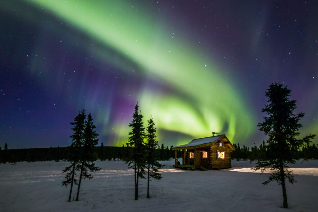 Green Northern Lights dance over a timber cabin in Alaska