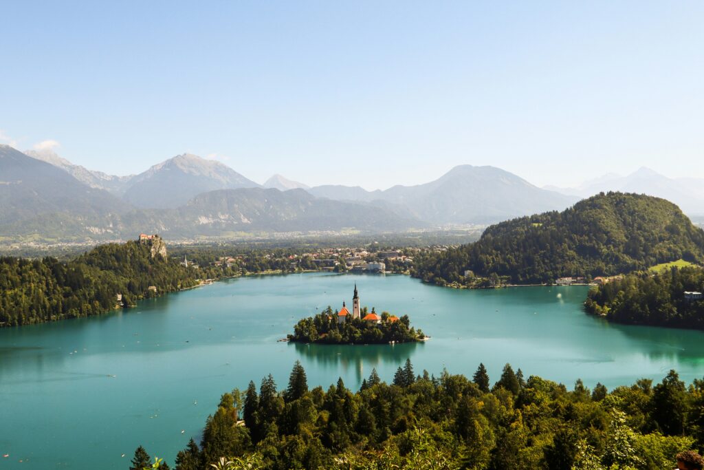 Large green coloured waters of Lake Bled in Slovenia, surrounded by Forrests and mountains.