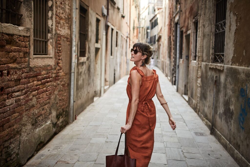 A woman in a brown linen sundress walks through a narrow street in Italy