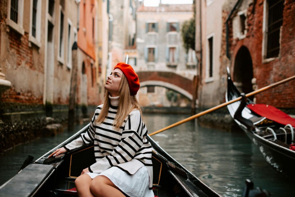 A woman sits in a gondola in Italy, wearing stylish clothing