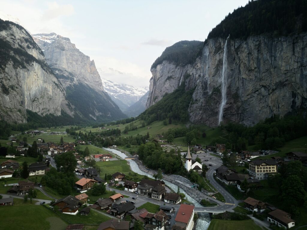 Alpine valley with sheer sided cliffs, with waterfall cascading down near a town