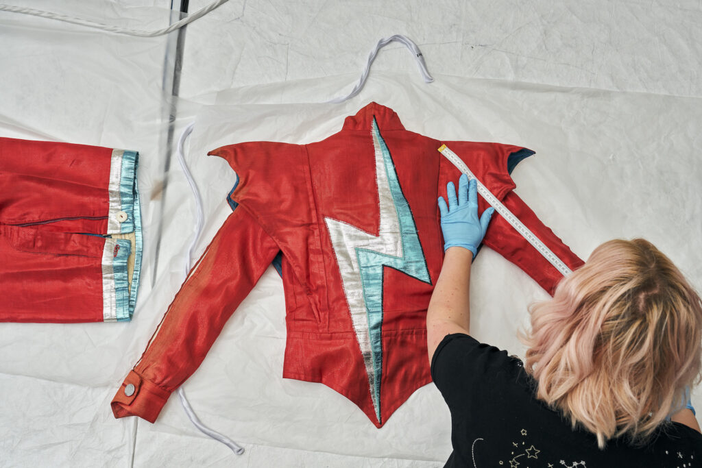 Overhead view of a museum worker measuring David Bowies costume