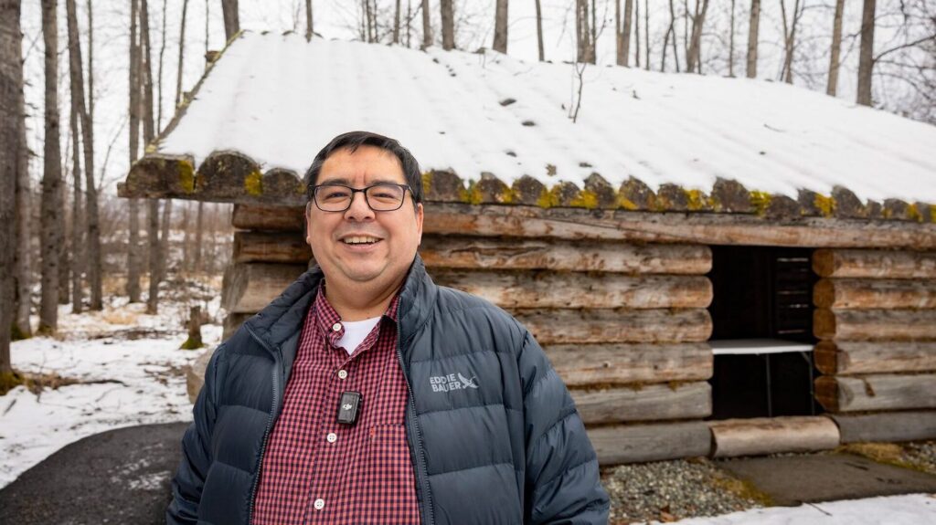 A man standing in front of a snow-covered log cabin