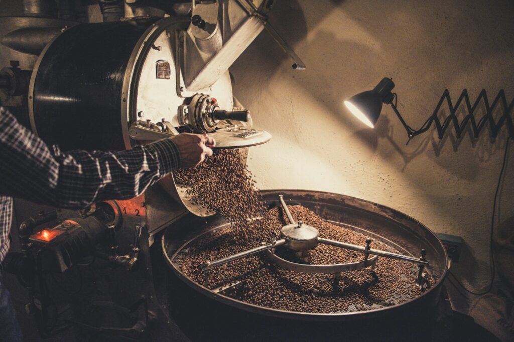 Man roasting coffee beans in a large metallic drum