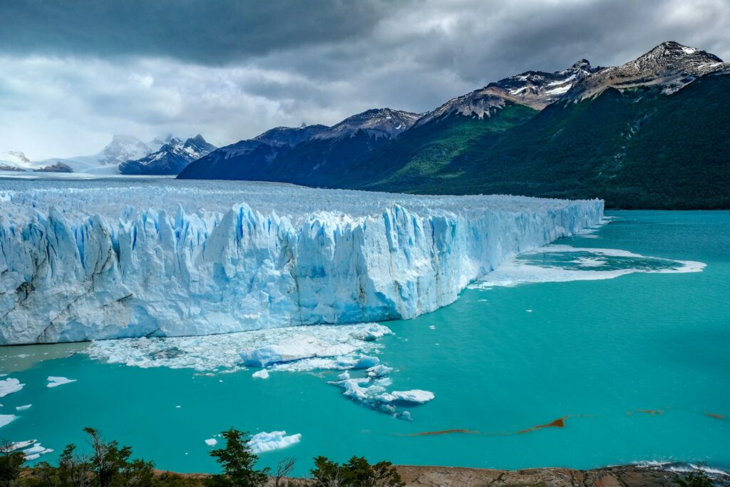 Wide angle view of glacier at the edge a blue lagoon, with mountains in the background