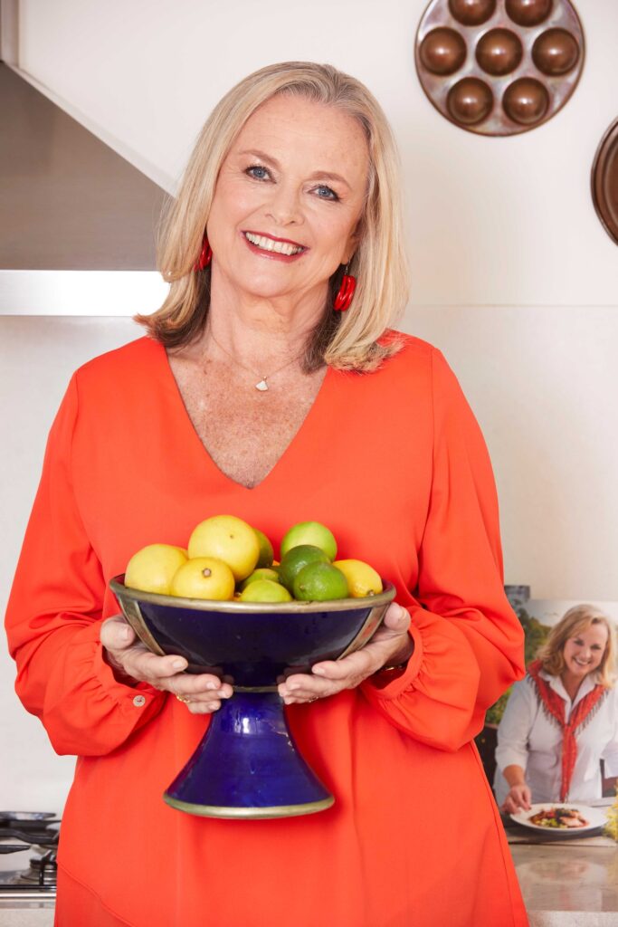 Lyndey Milan wearing an orange dress and holding a bowl of fruit