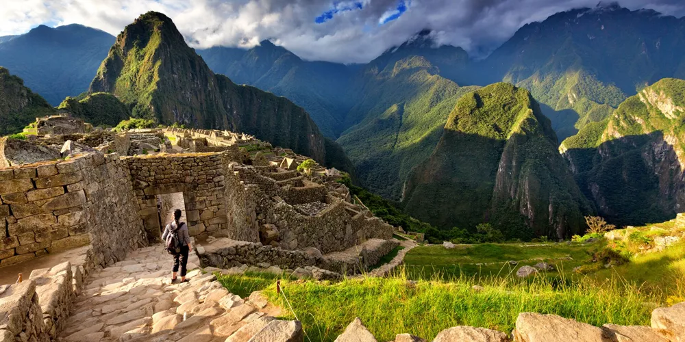 Back view of female tourist descending stairs overlooking Machu Picchu ruins at sunset, Peru
