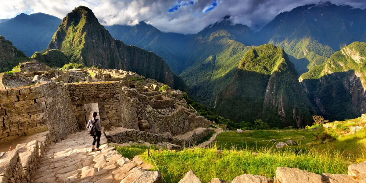 Back view of female tourist descending stairs overlooking Machu Picchu ruins at sunset, Peru