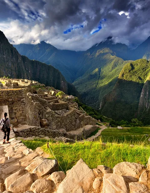 Back view of female tourist descending stairs overlooking Machu Picchu ruins at sunset, Peru