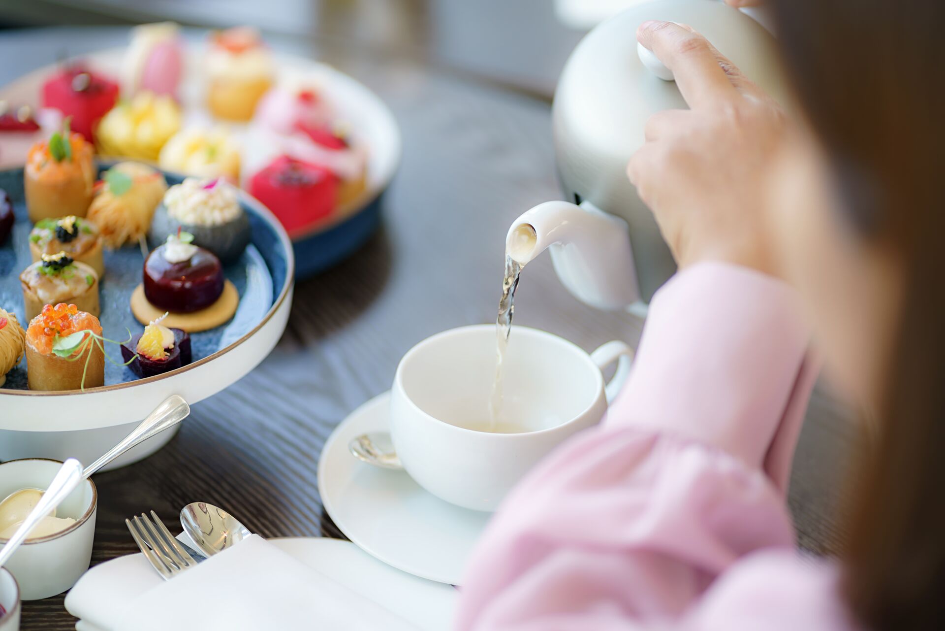 Woman pouring tea with desserts on the table in front of her