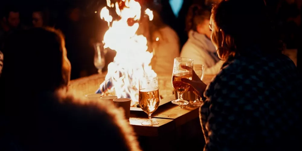 Friends sharing a mulled wine while looking at a bonfire during Hogmanay in Scotland, UK