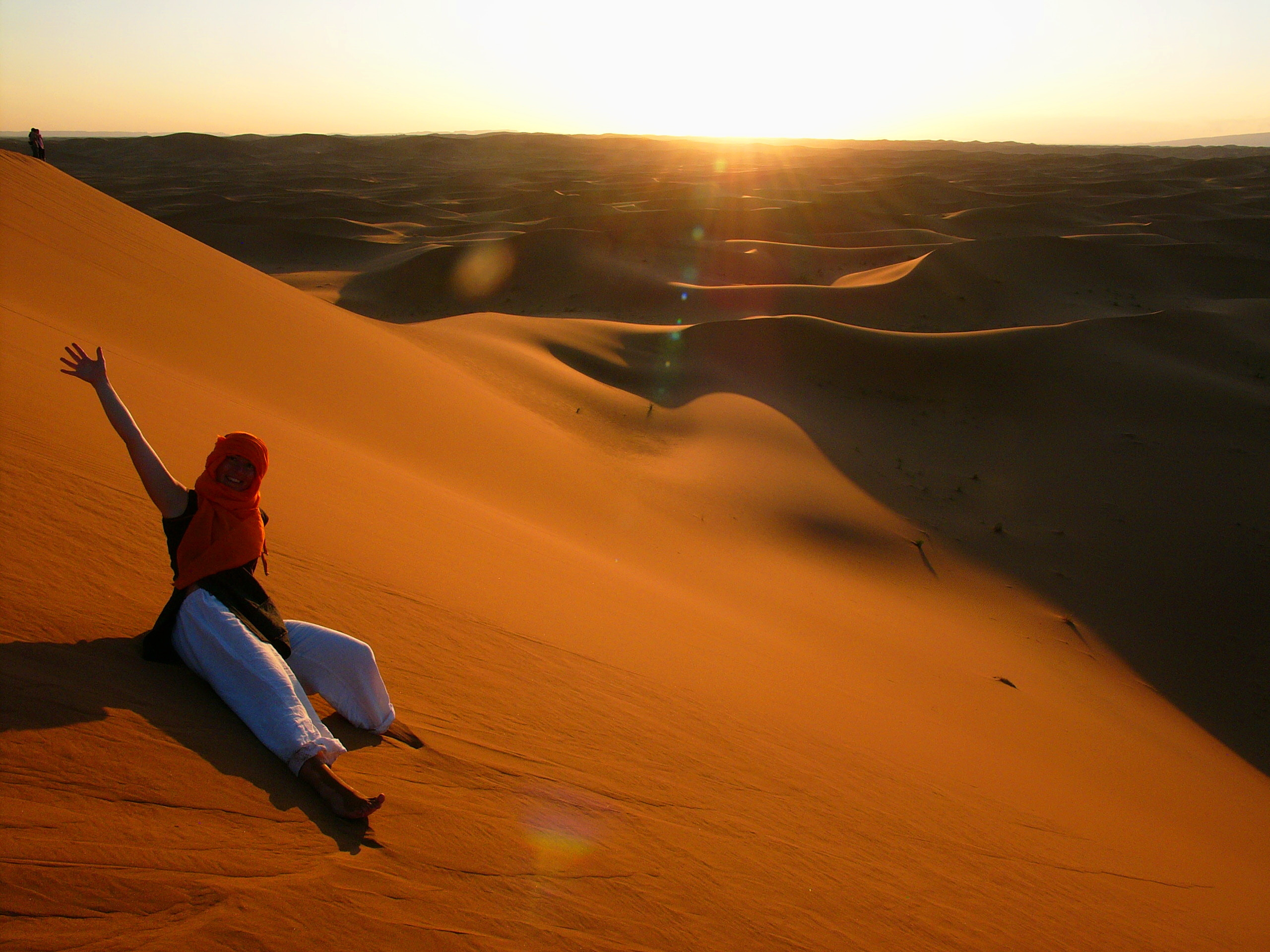 Smiling Young Woman With Arm Raised Sitting On Sand Dune During Sunny Day 674746141