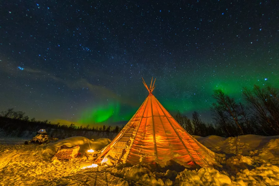 A tipi in Sweden with the Northern Lights shining behind it