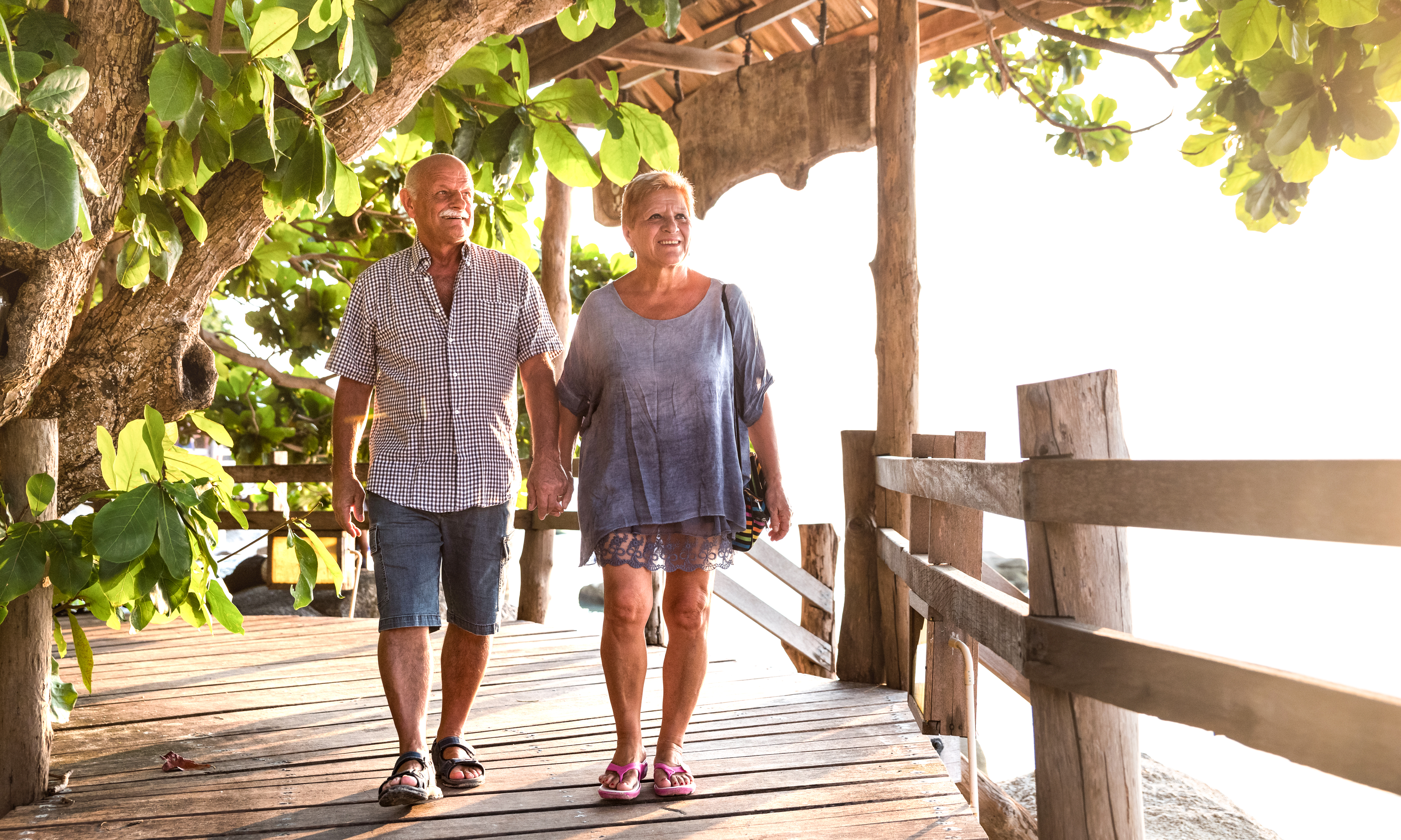 Happy Senior Couple Walking And Holding Hands At Koh Phangan Beach Promenade