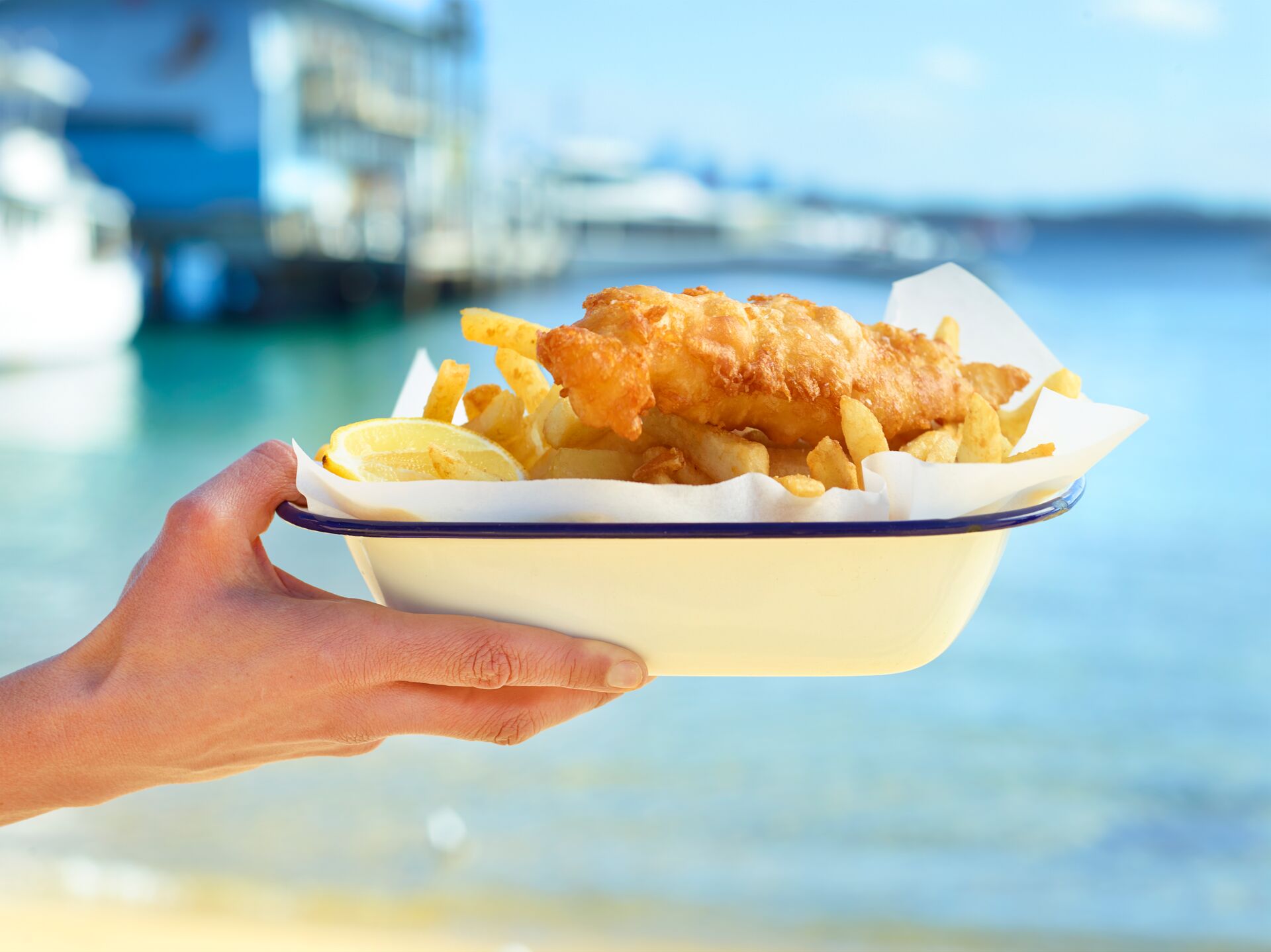 Woman holding up a plate of fish and chips on a sunny day