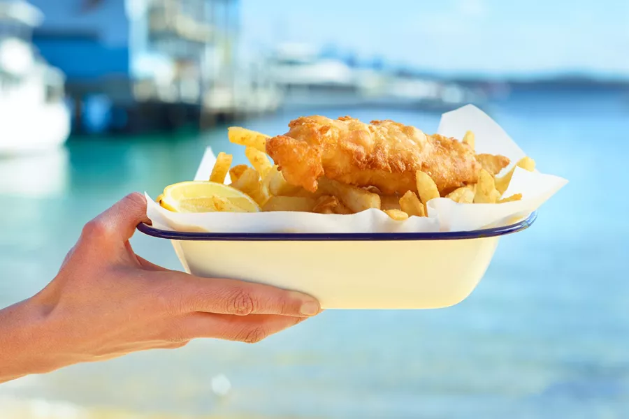 Woman holding up a plate of fish and chips on a sunny day