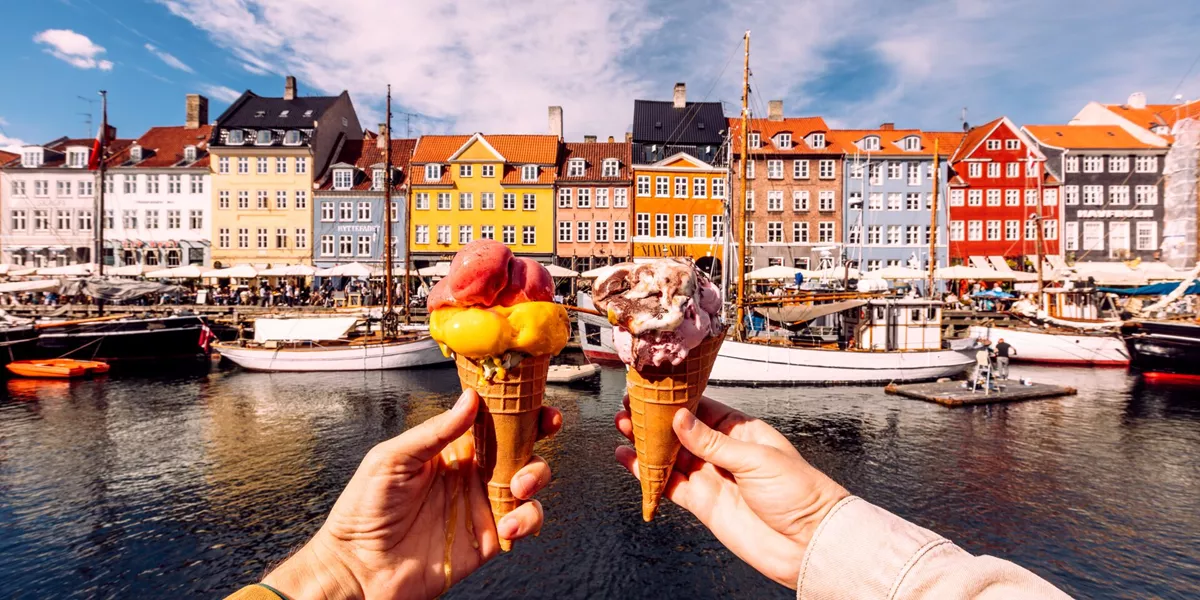 2 people holding up ice cream infront of some colourful houses in Copenhagen, Denmark