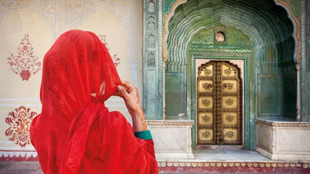 Woman in red scarf looking at green gate door in City Palace of Jaipur, Rajasthan, India
