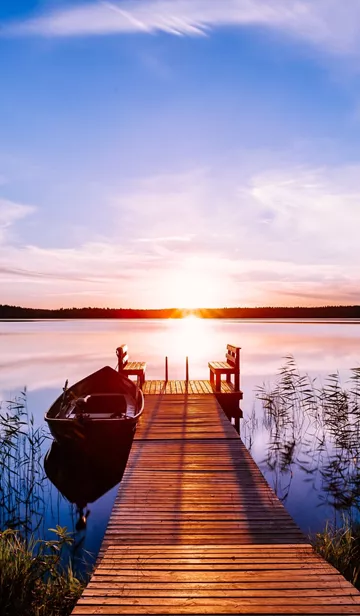 Wooden pier with fishing boat at sunset on a lake