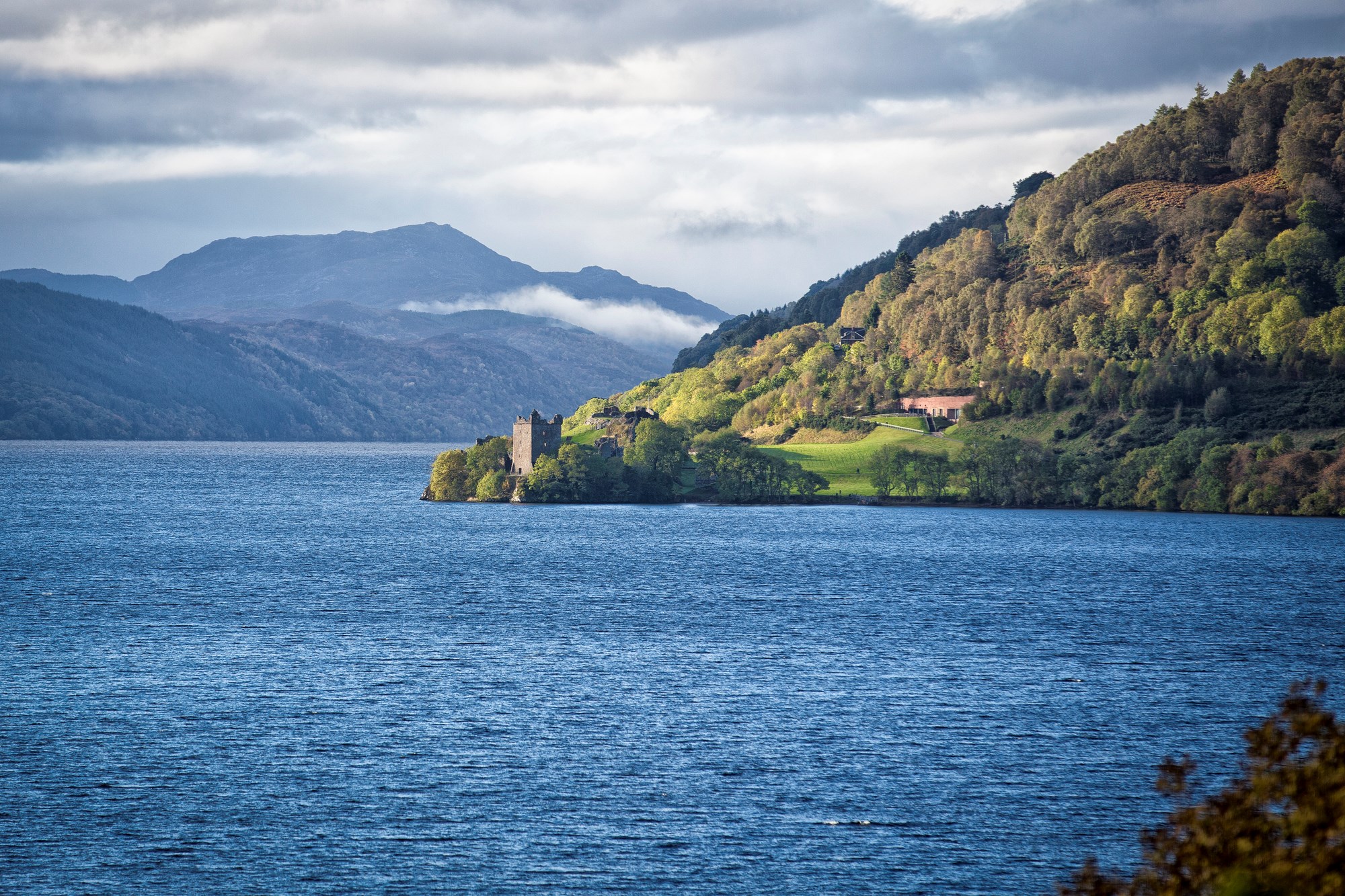 Urquhart Castle ruins on green hillside overlooking deep blue waters of Loch Ness