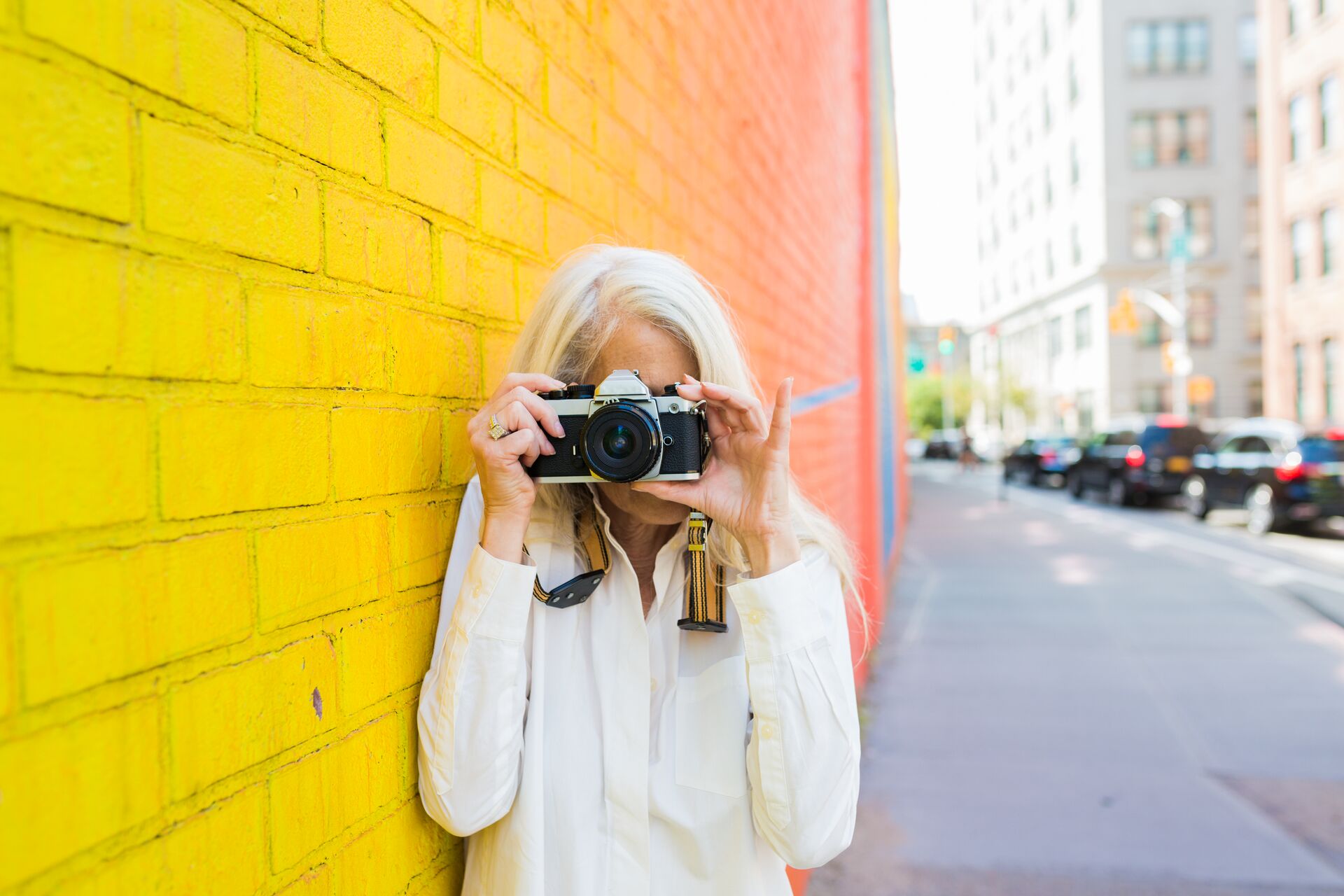 Mature woman leaning against a wall taking picture with a camera